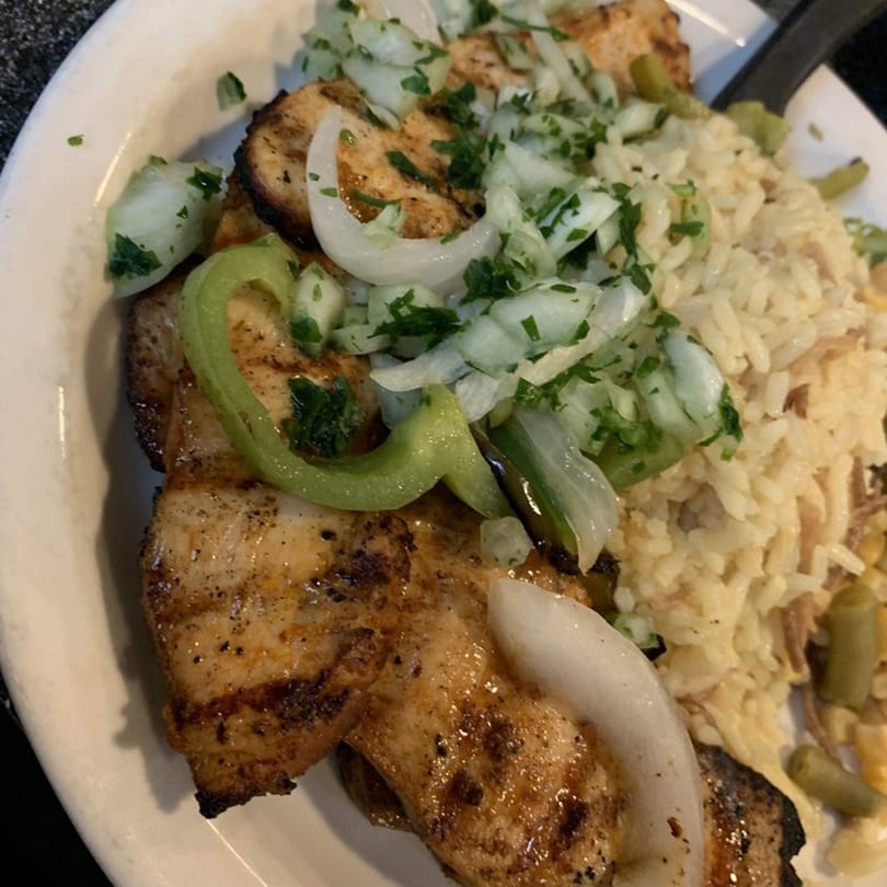 Grilled chicken kebab with rice, topped with chopped onions, green peppers, and parsley.