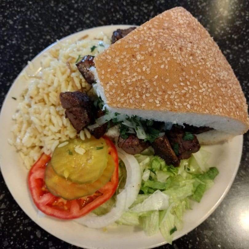 George's Shish Kebab plate with rice, kebab sandwich, lettuce, tomato, onion, and pickles.